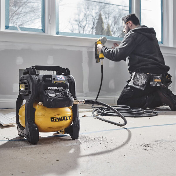 A man using a DeWalt cordless air compressor to drill a window.