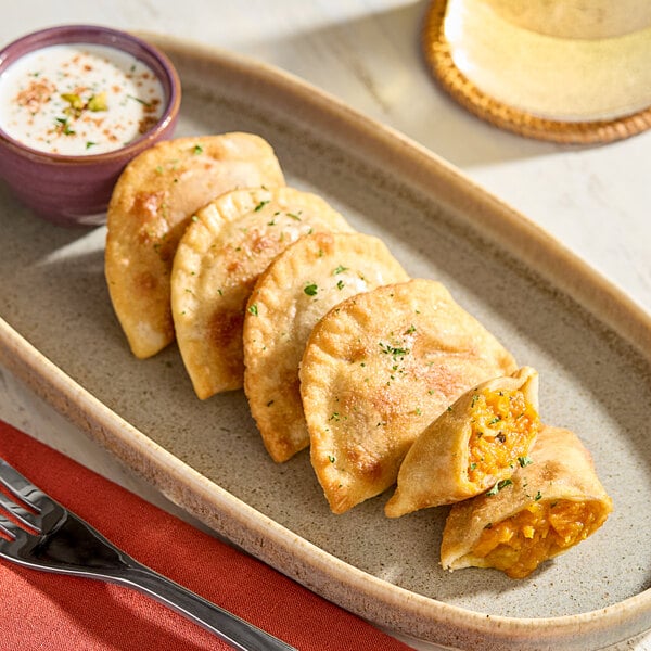 A plate of Jaju Butternut Squash, Apple, and Sage Pierogies with a bowl of dipping sauce on a table.