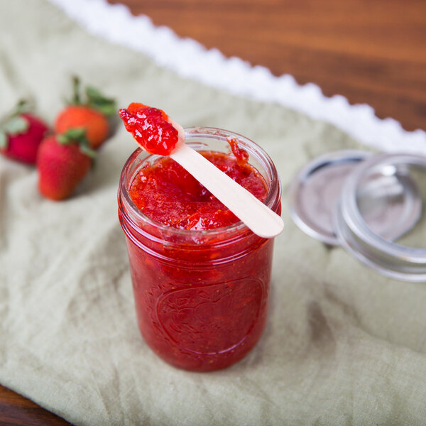 A jar of red jam with a wooden Eco-gecko taster spoon in it.