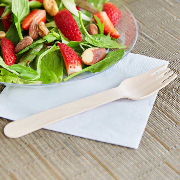 A salad with strawberries and nuts on a plate with a wooden Eco-gecko fork.