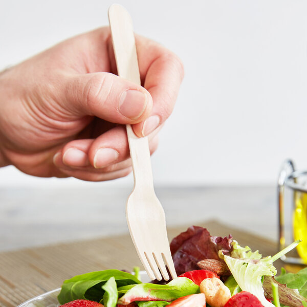 A person holding an Eco-gecko wooden fork over a salad.