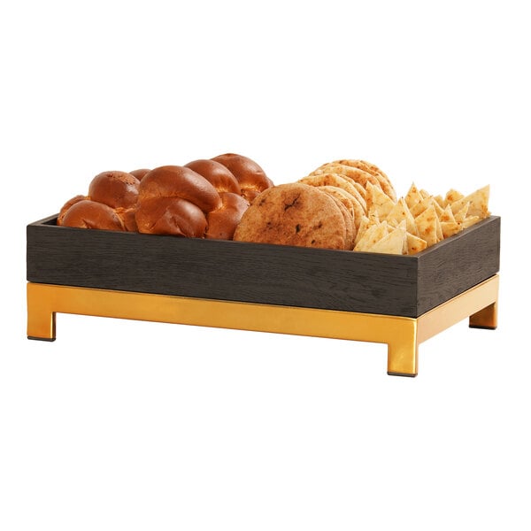 A Cal-Mil brass metal display riser holding a tray of bread, cookies, and other snacks.
