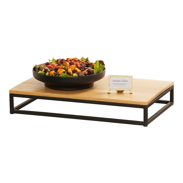 A black metal rectangular display riser with a bowl of salad on a table.