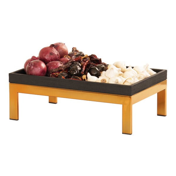 A Cal-Mil brass display riser with a tray of red onions and vegetables.