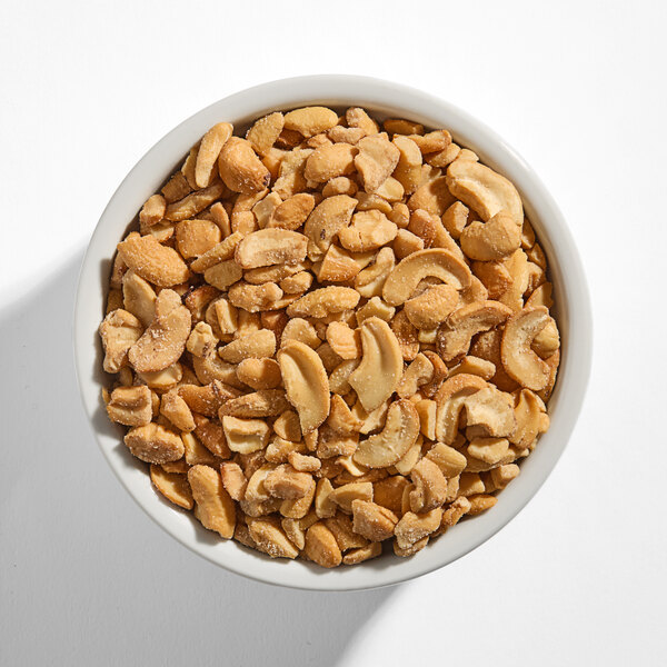 A white bowl filled with large roasted salted cashew pieces.