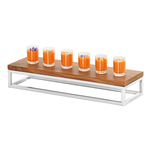 A row of Cal-Mil display risers with glasses of orange liquid on a wood table.