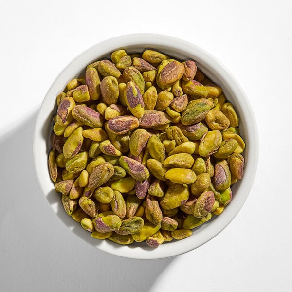 A white bowl filled with raw pistachio halves.