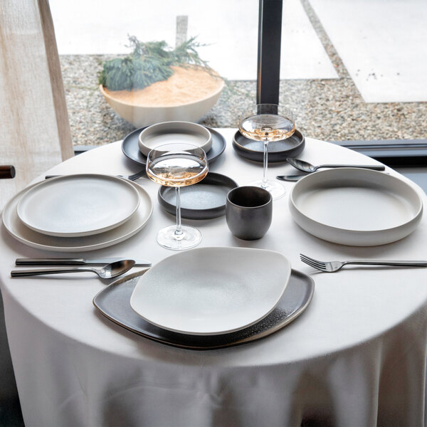 An 8 1/2 inch volcanic gray round raised rim coupe stoneware plate from the Cloud Terre by Fortessa Iceland collection, shown as part of a modern table setting.
