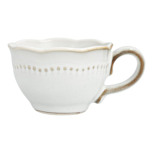 A white stoneware espresso cup with a scalloped edge and embossed pearl dots and brown trim.