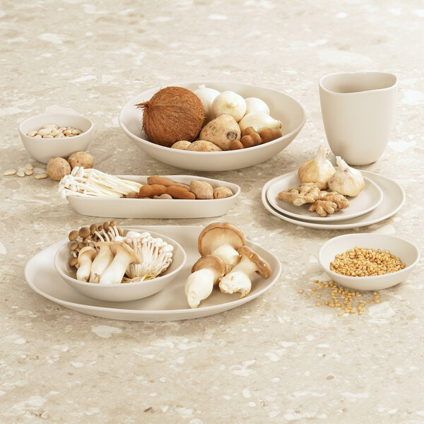 A set of ivory round melamine plates displayed with various foods on a stone surface.