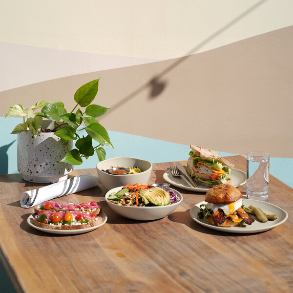 A round ivory melamine plate displayed on a wooden table with food and other dishes.