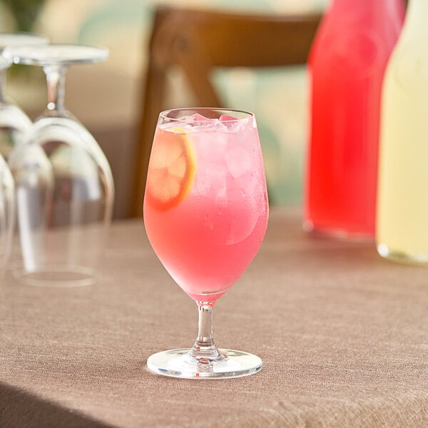 A glass of pink drink with a slice of lemon on a table.
