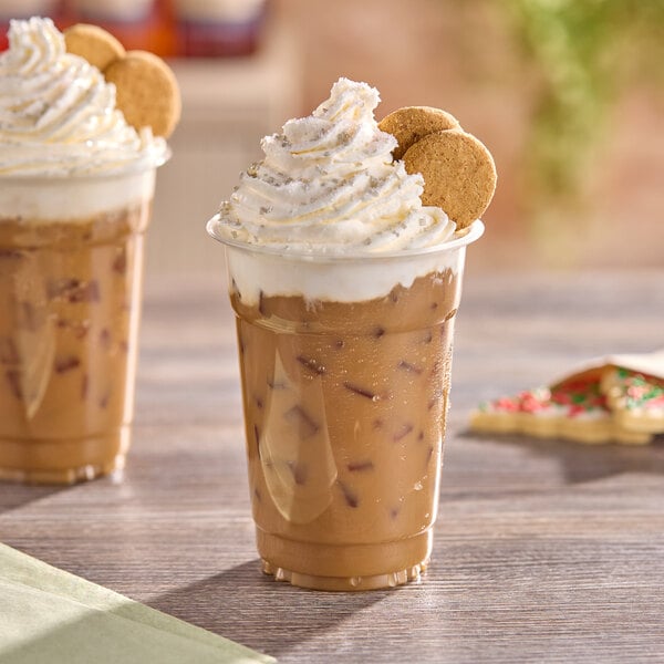 A plastic cup filled with iced coffee topped with whipped cream and two small cookies.
