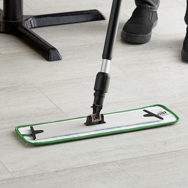 A person using a Lavex green microfiber mop pad on a mop handle to clean a floor.