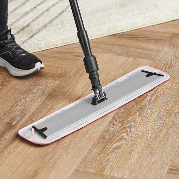 A person using a Lavex 24" pink microfiber mop pad with a handle to clean a wood floor.