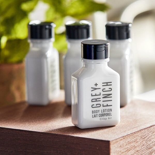A group of small white Grey + Finch body lotion bottles with black lids on a table.