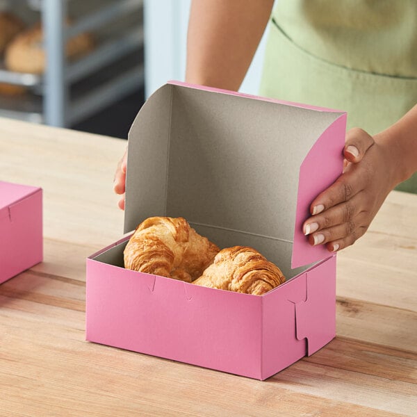 A pink bakery box containing two croissants on a wooden surface.