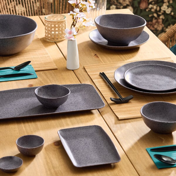 A set of dark gray round melamine bowls and plates arranged on a wooden dining table.