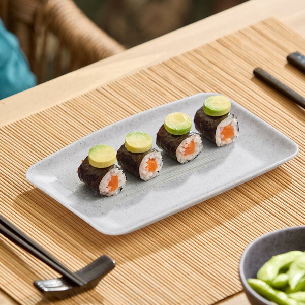 A light gray rectangular melamine platter displaying four pieces of sushi, shown on a bamboo placemat.