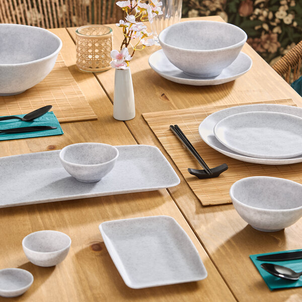 A set of light gray round melamine ramekins displayed on a wooden dining table with matching dinnerware.