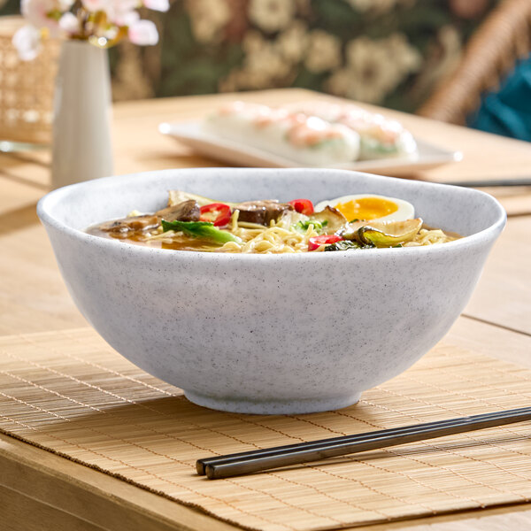 A large, light gray round melamine bowl filled with ramen, shown on a table setting.