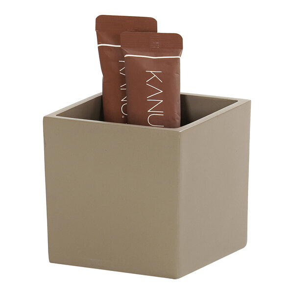 A taupe square resin crock holding small brown packets.