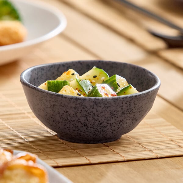 A small dark gray round melamine bowl filled with a cucumber salad.
