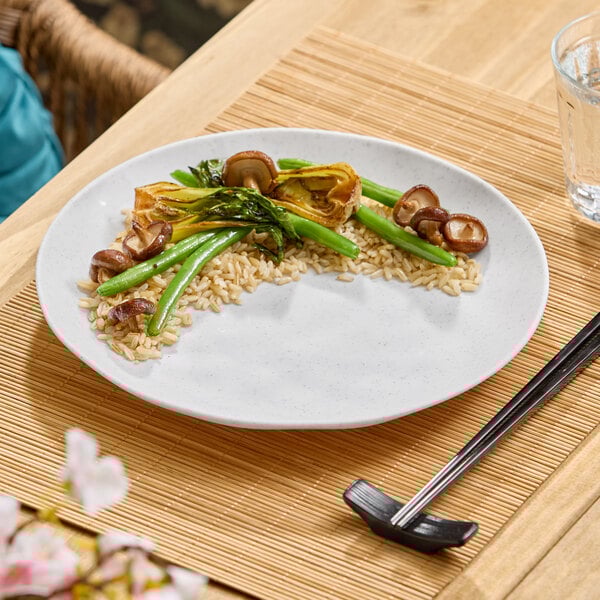 A white round melamine plate with a partial serving of rice, green beans, mushrooms, and other vegetables arranged on it.