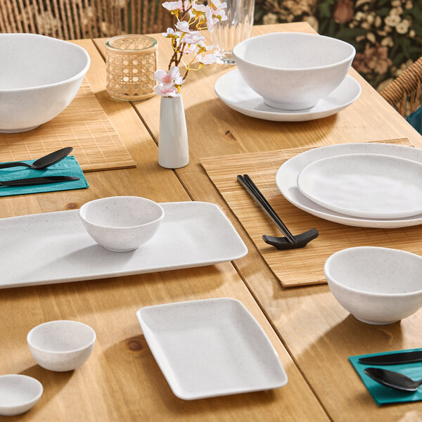 A set of white round melamine plates displayed on a wooden dining table with other tableware and utensils.