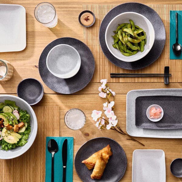 A white round melamine plate measuring 7 3/4 inches, shown as part of a table setting with various dishes and utensils.
