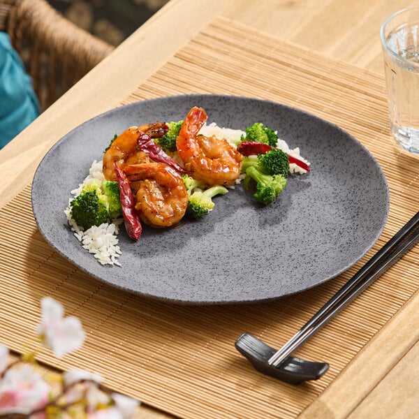 A dark gray round melamine plate with a serving of shrimp, broccoli, rice, and dried red peppers.