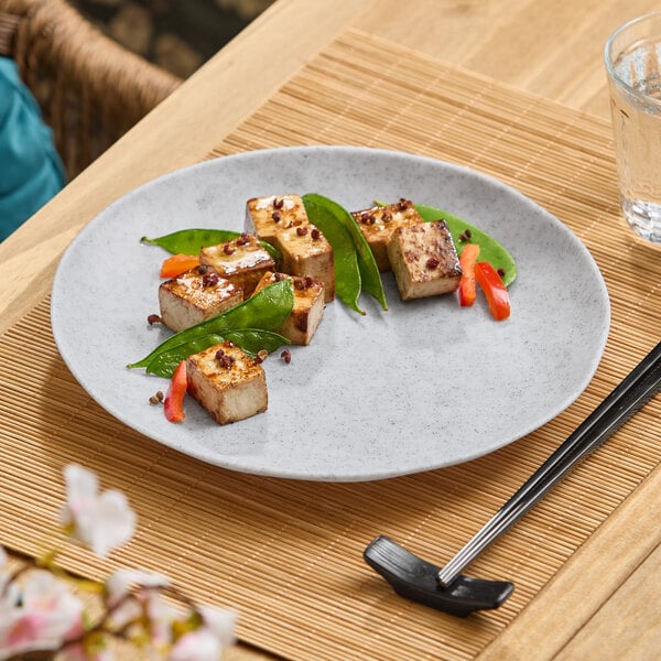 A light gray melamine plate with grilled tofu cubes, snap peas, and red pepper strips arranged on it.