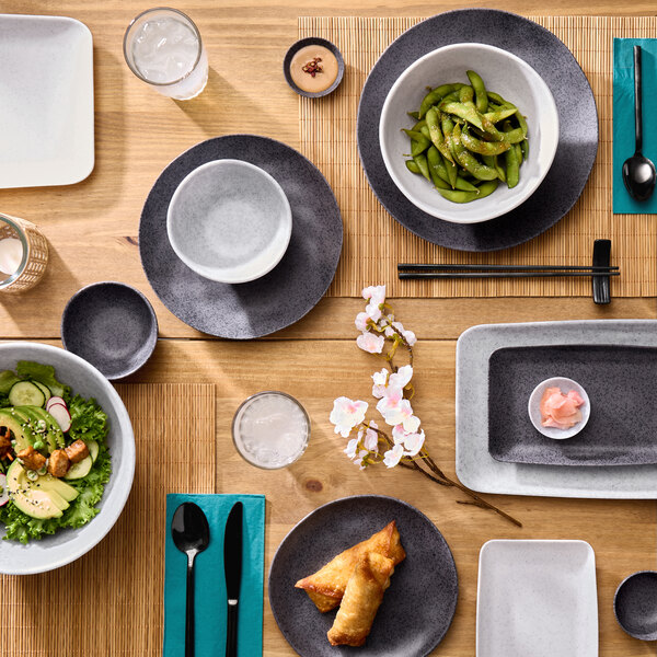 A white rectangular melamine platter displayed on a wooden table set with various dishes and utensils.