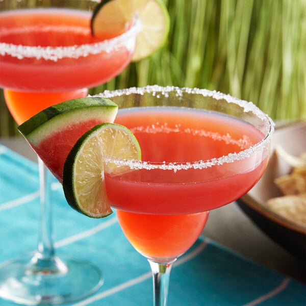 A close-up of a watermelon and lime drink with a lime wedge on the rim.
