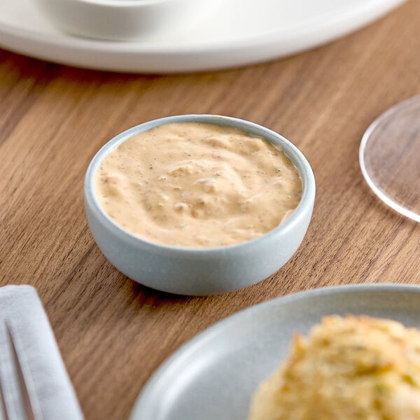 A bowl of Ken's Signature Remoulade Sauce on a table with food.