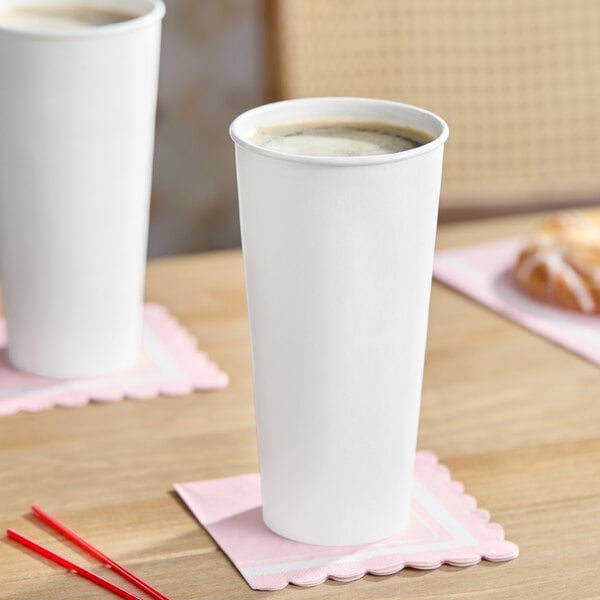 A white 24 oz. double wall insulated paper hot cup filled with a beverage, placed on a pink napkin.