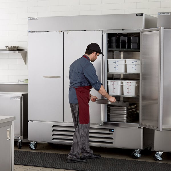 A man in a red apron opening a Beverage-Air Horizon Series reach-in freezer with solid doors.