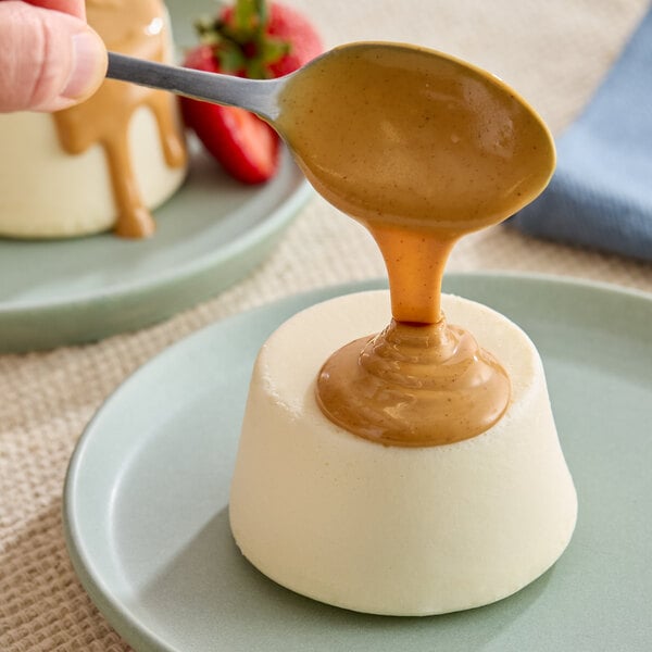 A plate of panna cotta dessert being topped with a thick peanut butter sauce from a spoon.