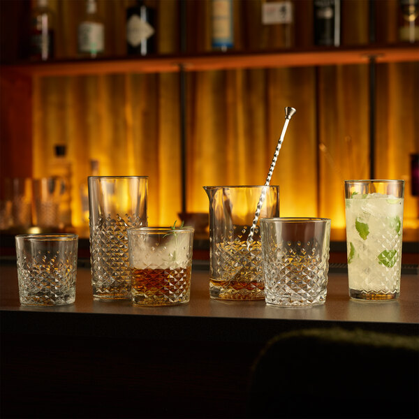 A set of textured glassware including rocks and highball glasses displayed on a bar counter.