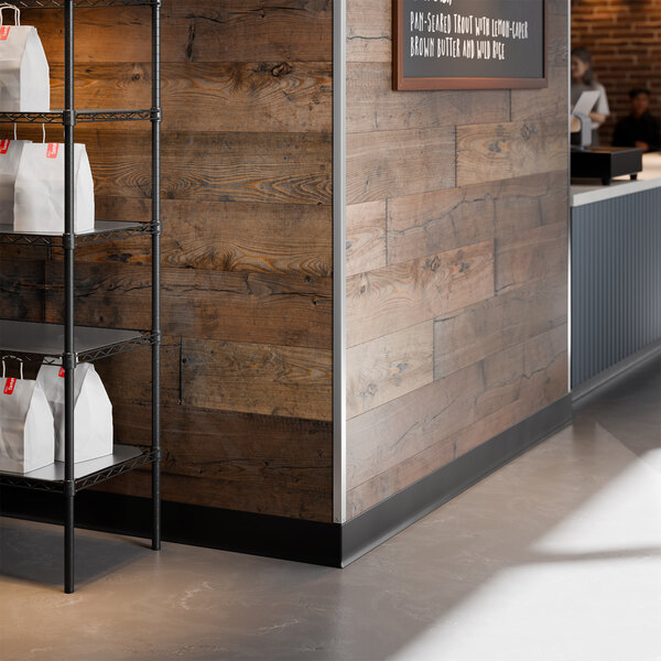 A stainless steel wall corner guard installed on the corner of a wooden wall in a commercial setting.