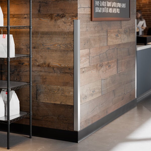 A stainless steel wall corner guard with adhesive strips installed on the corner of a wooden wall.