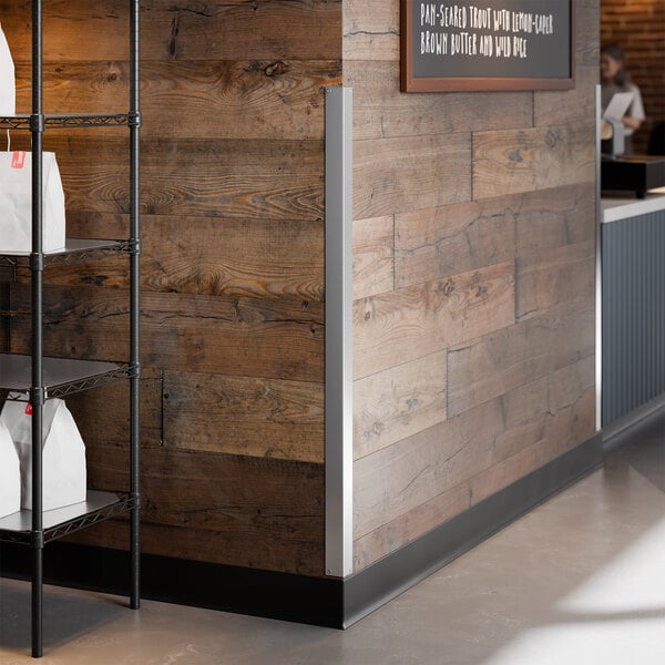 A stainless steel wall corner guard with mounting holes installed on the corner of a wooden wall.