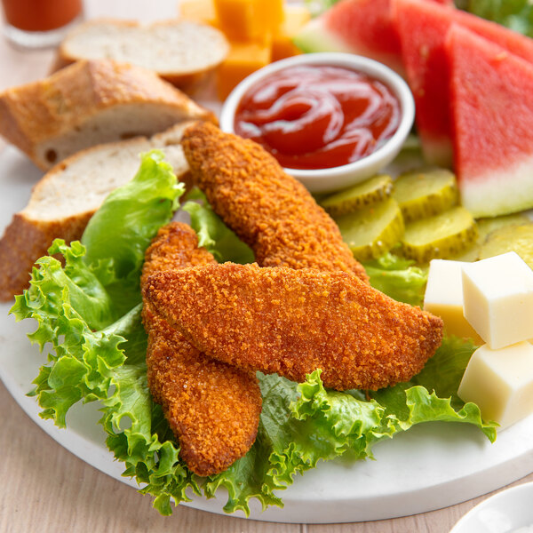 A white plate with breaded chicken tenders and lettuce with a bowl of ketchup.
