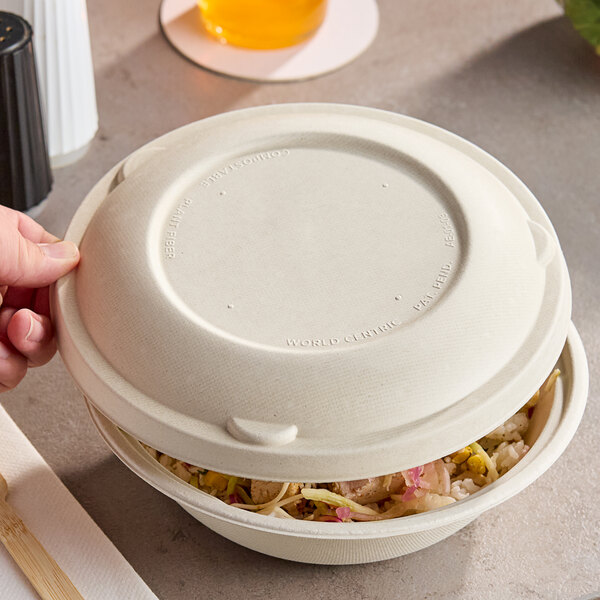 A compostable fiber lid being placed on a wide take-out bowl filled with food.