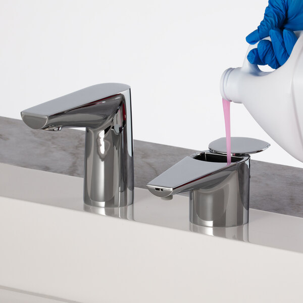 A person pouring pink liquid into a faucet with a Bobrick polished chrome deck-mount automatic liquid soap dispenser.