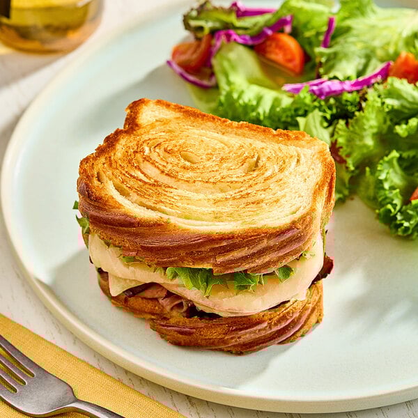 A sandwich made with sliced pure butter flaky bread loaf, served with a side salad.