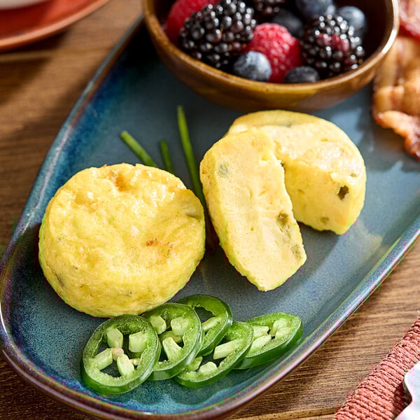 A plate with two cheese and jalapeno egg bites, accompanied by sliced jalapenos and a bowl of mixed berries.