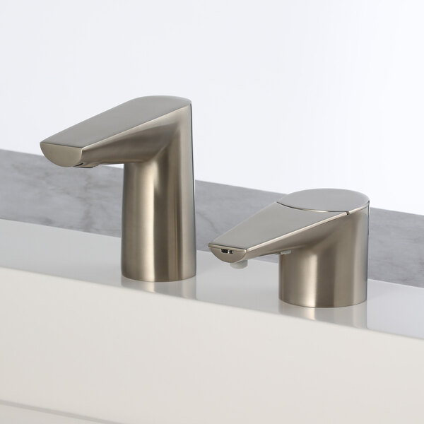 A Bobrick brushed nickel deck-mount soap dispenser on a white counter next to two faucets.