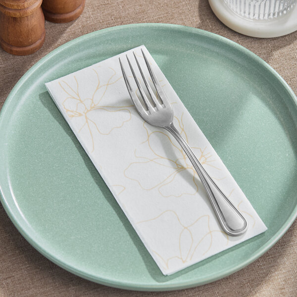 A linen-feel guest towel with a subtle flower design folded on a green plate with a fork on top.