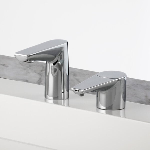 Two Bobrick polished chrome deck-mount automatic faucets on a white counter.
